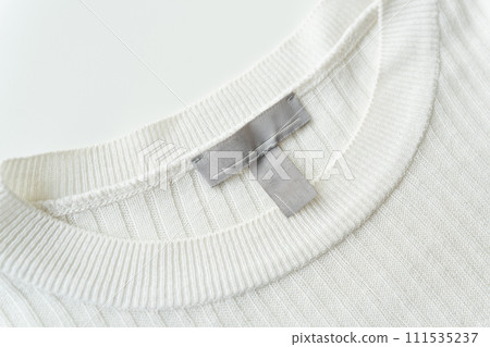 Close-up of a white knitted sweater neckline with a grey tag, highlighting fabric texture and quality. 111535237
