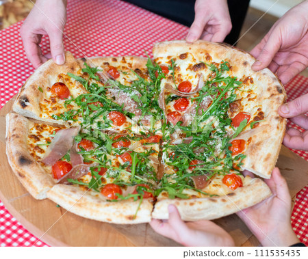 Pizza with ham and vegetables on wooden table sharing hands Pizza with ham and vegetables on wooden table sharing hands 111535435