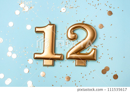 Gold candles in the form of number twelve on blue background with confetti. 12 years celebration. Gold candles in the form of number twelve on blue background with confetti. 12 years celebration. 111535617