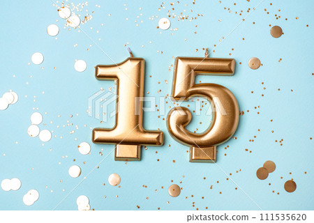 Gold candles in the form of number fifteen on blue background with confetti. 15 years celebration. 111535620