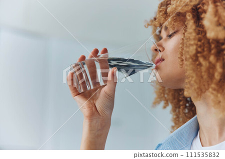 Woman with curly hair enjoying a refreshing drink of water from a glass in a healthy lifestyle concept 111535832