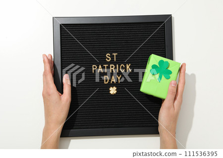 Black letters board with golden letters, box with clover leaf and hands on white background, top view 111536395
