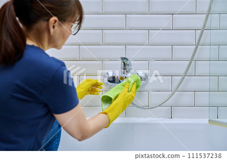 Woman cleaning bathroom, washing faucet, tile with professional cloth, foam cleaner Woman cleaning bathroom, washing faucet, tile with professional cloth, foam cleaner 111537238