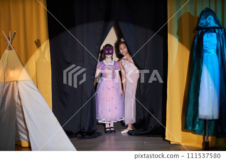 Full length portrait of two little girls entering stage in theater opening curtain with spotlight on 111537580