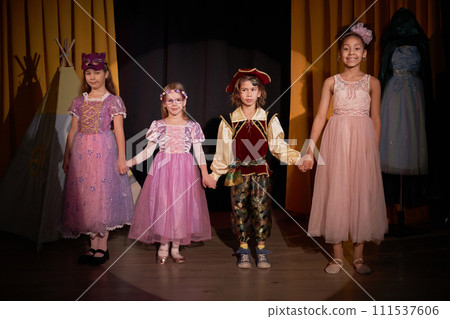 Full length portrait of group of children actors standing on stage holding hands for final bow at school play in theater Full length portrait of group of children actors standing on stage holding hands for final bow at school play in theater 111537606