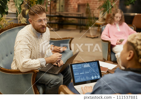 Portrait of bearded man wearing glasses while talking to colleague and collaborating on project in vintage coworking space 111537881