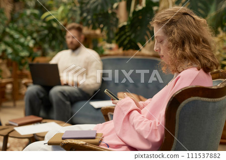 Side view portrait of young woman wearing pink and using mobile phone in green office copy space Side view portrait of young woman wearing pink and using mobile phone in green office copy space 111537882