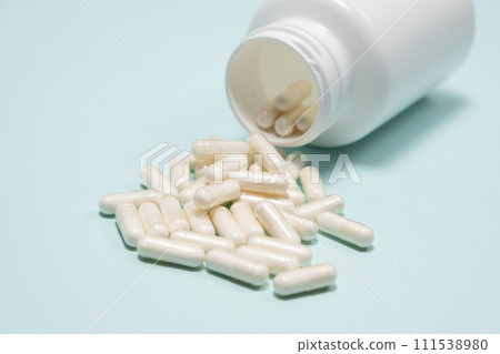 White medicine capsules spilled out of a jar on light blue background close-up. White medicine capsules spilled out of a jar on light blue background close-up. 111538980