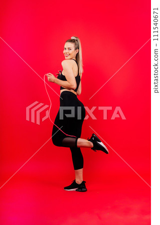 Fitness woman doing jumping exercises with skipping rope on colorful yellow red background. 111540671
