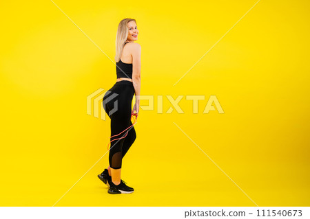 Fitness woman doing jumping exercises with skipping rope on colorful yellow red background. 111540673