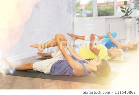 Preteen boy practicing knee to chest pose of yoga in light fitness room Preteen boy practicing knee to chest pose of yoga in light fitness room 111540862