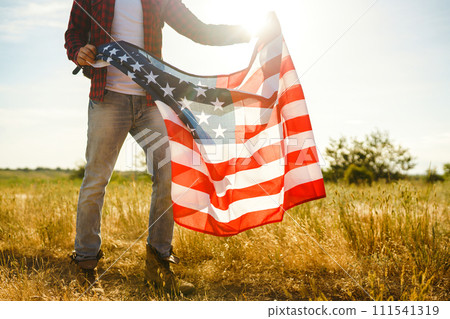 4th of July. American Flag. Traveler with the flag of America. The man in a hat, a backpack, a shirt and jeans. 4th of July. American Flag. Traveler with the flag of America. The man in a hat, a backpack, a shirt and jeans. 111541319