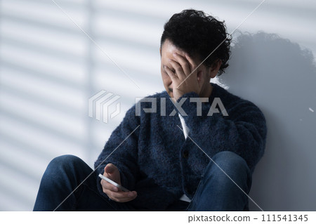 Close-up of a sad or worried man looking at his smartphone with his shoulders down, no face covering his face with his hands 111541345