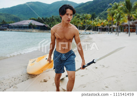 Serene Summer Fun: Asian Man Enjoying Kayaking Adventure on Tropical Beach Serene Summer Fun: Asian Man Enjoying Kayaking Adventure on Tropical Beach 111541459