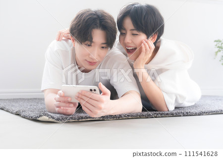 Couple lying down in the living room while watching a movie on their smartphone, close-up 111541628