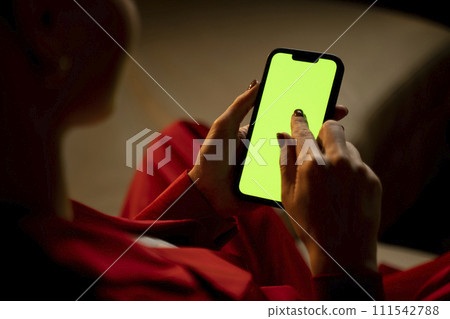 Woman Holding a Smartphone With Green Screen in a Dimly Lit Room at Night Woman Holding a Smartphone With Green Screen in a Dimly Lit Room at Night 111542788