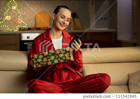 Woman in Red Pajamas Relaxing on Couch With Smartphone at Home During Evening Woman in Red Pajamas Relaxing on Couch With Smartphone at Home During Evening 111542845