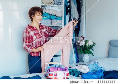 Woman selecting clothes from her wardrobe for donating to a Charity shop. Decluttering, Sorting clothes and Cleaning Up. Reuse, second-hand concept. Conscious consumer, sustainable lifestyle. 111543531