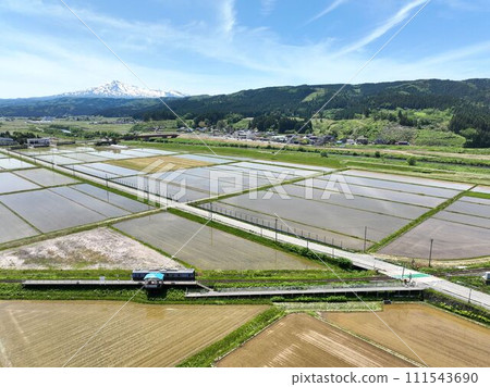 Aerial footage of a train near Magarisawa Station on the Yuri Kogen Railway Chokaisanroku Line, with Mount Chokai in the background. 111543690