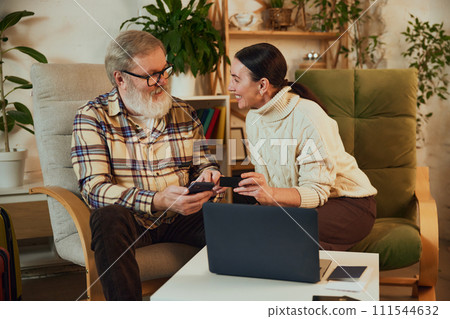 Elderly couple, man and woman sitting at home and buying tickets online, booking hotel and paying online with credit card. Payment app Elderly couple, man and woman sitting at home and buying tickets online, booking hotel and paying online with credit card. Payment app 111544632