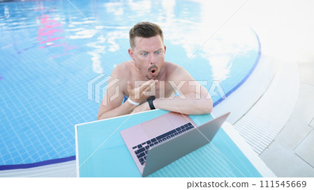 Shocked young man in the pool looks into a laptop 111545669