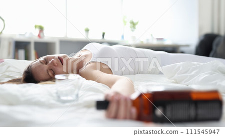 Drunk woman sleeps alone on a bed with a bottle 111545947
