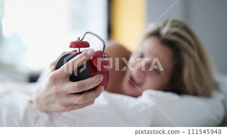 Screaming woman in bed with a red alarm clock in her hand 111545948