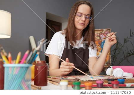 Artistic talent workshop. Painter's creative studio. Artwork inspiration session. Caucasian woman painter wearing brown apron in art studio drawing picture Artistic talent workshop. Painter's creative studio. Artwork inspiration session. Caucasian woman painter wearing brown apron in art studio drawing picture 111547080