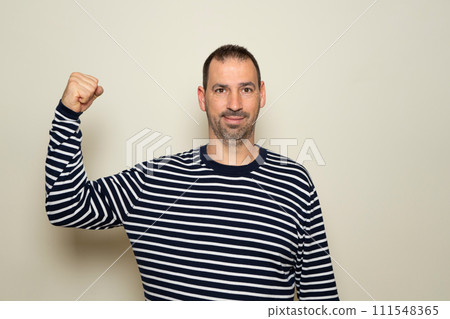 Hispanic man with a beard of 40 years old showing biceps believing that his training has paid off, the poor deluded man does not realize his terrible physical condition. Isolated beige background. 111548365