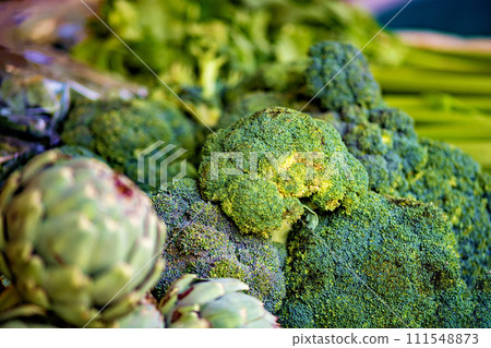 Pile of broccoli sitting on top of table next to other vegetables 111548873