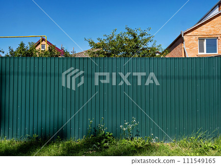 Green fence in front of brick building on sunny day. Green fence in front of brick building on sunny day. 111549165