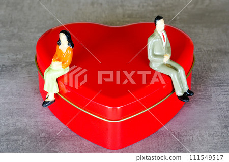 Quarrelled female and male toy figures sit on different sides of a large red heart shape figure Quarrelled female and male toy figures sit on different sides of a large red heart shape figure 111549517