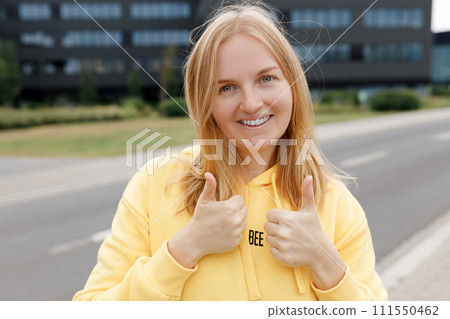 Image of a happy optimistic emotional young student posing over city background dressed casual, showing thumbs up gesture. Lifestyle concept. 111550462