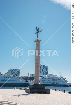 A statue with outstretched wings atop a column overlooks a promenade by the sea, with a FORSEA ferry and modern checkered buildings, likely in Helsingborg. 111550586