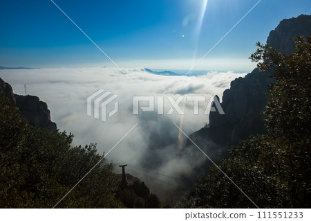 A scenic view from a high point near Barcelona, Spain, showcasing a sea of clouds flowing through mountains, with sunlight creating a lens flare and a utility pole hinting at human touch. A scenic view from a high point near Barcelona, Spain, showcasing a sea of clouds flowing through mountains, with sunlight creating a lens flare and a utility pole hinting at human touch. 111551233