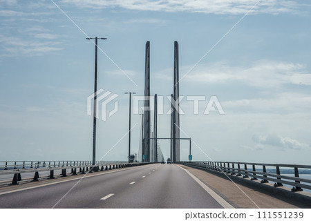 A modern, multilane Oresund Bridge under a clear sky connects Copenhagen, Denmark, with Malmo, Sweden, featuring tall pylons and a sleek cablesupported design. 111551239