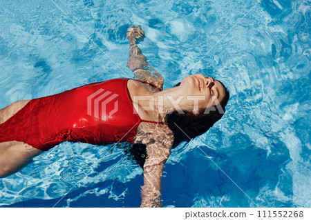Happy woman swimming in pool in red swimsuit with loose long hair, skin protection with sunscreen, concept of relaxing on vacation. Happy woman swimming in pool in red swimsuit with loose long hair, skin protection with sunscreen, concept of relaxing on vacation. 111552268