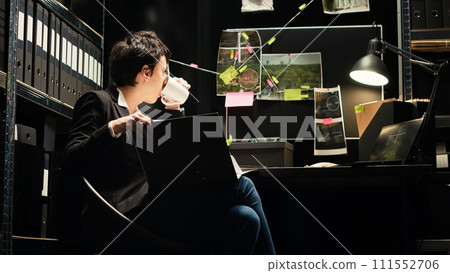 Detective evaluates confidential police files to undertake investigatory law services, working in incident room. Criminal expert reviewing crime details, reads witness statements. Handheld shot. 111552706