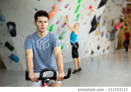 Young man riding exercise bike in climbing gym Young man riding exercise bike in climbing gym 111553115
