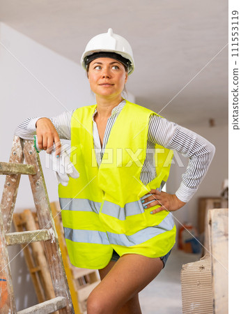 Young woman with naked legs in safety vest and construction helmet posing in apartment during overhauls 111553119