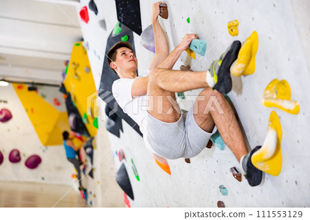 Male mountaineer climbing artificial rock wall without his belay indoors Male mountaineer climbing artificial rock wall without his belay indoors 111553129