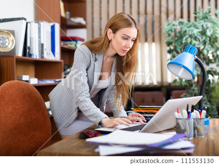 Portrait of a young business woman in the office, typing an document on a laptop 111553130