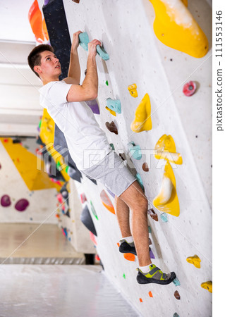 Male mountaineer climbing artificial rock wall without his belay indoors Male mountaineer climbing artificial rock wall without his belay indoors 111553146