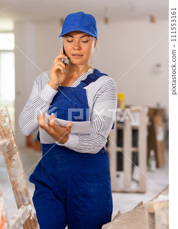 Female worker in blue overall discussing repair plan on mobile phone 111553161