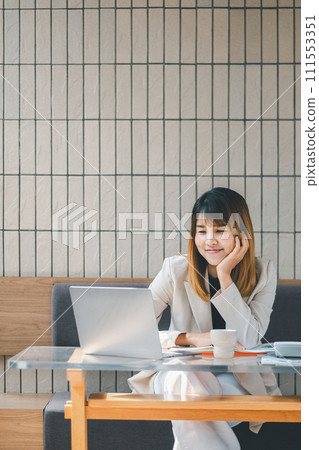 Freelancer concept, A content businesswoman in a stylish beige jacket typing on her laptop at a wooden cafe table, with a smartphone beside her. Freelancer concept, A content businesswoman in a stylish beige jacket typing on her laptop at a wooden cafe table, with a smartphone beside her. 111553351