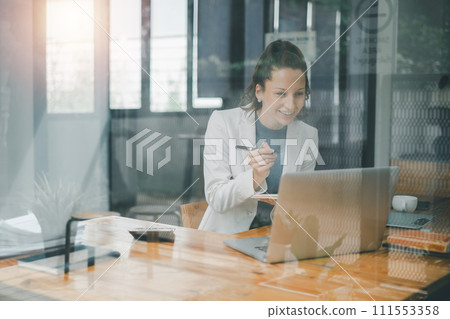 Business analyticsconcept, Smiling professional woman engaged in work on her laptop at a wooden desk in a well-lit office environment. Business analyticsconcept, Smiling professional woman engaged in work on her laptop at a wooden desk in a well-lit office environment. 111553358