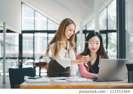 Business team analytics concept, Two engaged female colleagues discussing work projects on a laptop in a bright modern office setting. 111553364