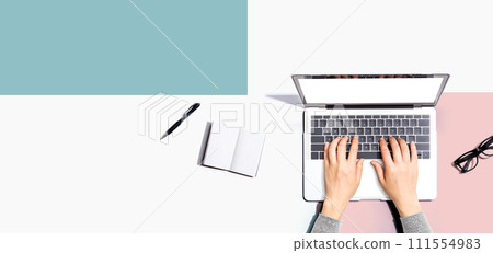 Person using a laptop computer with a notebook and eyeglasses 111554983