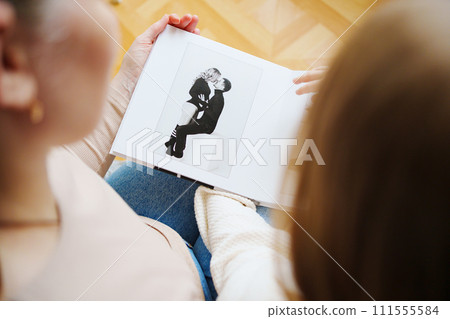 mother and daughter flips through a book with photos of dad and pregnant mom. mother and daughter flips through a book with photos of dad and pregnant mom. 111555584