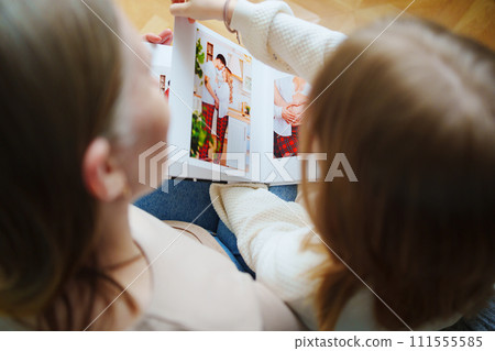 mother and daughter flips through a book with photos of dad and pregnant mom. 111555585